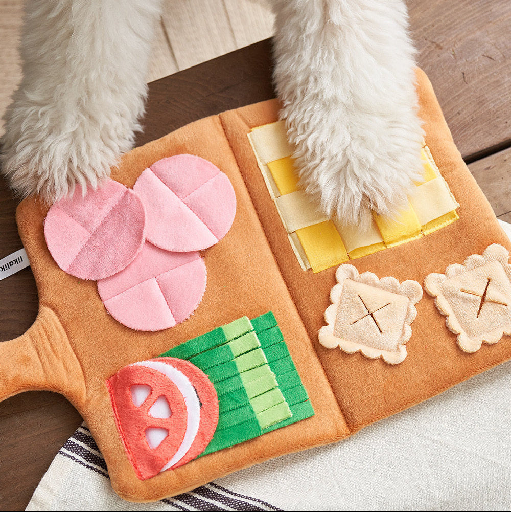 Dog playing with a toy shaped like a pizza on a wooden floor.